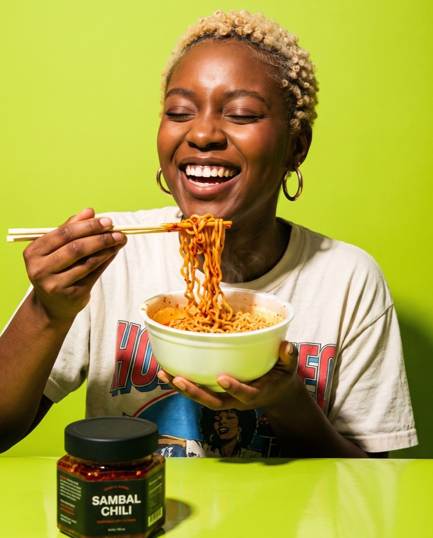 Zola Whitfield laughing while lifting chili-oiled noodles out of a bowl.